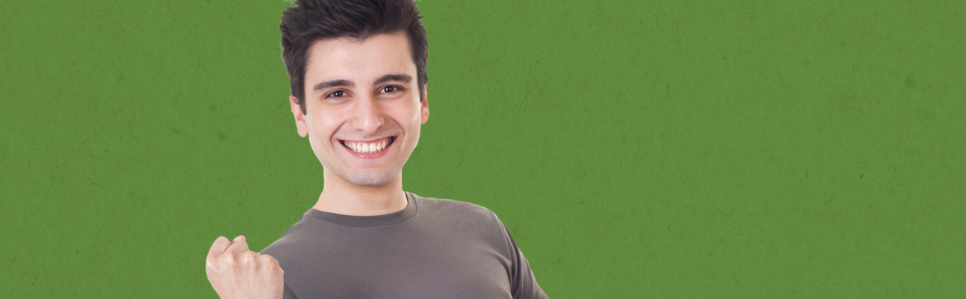 Young boy smiling and wearing a grey tshirt in front of a solid green background.