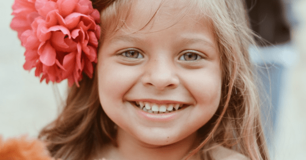 Young girl smiling with a red flower in her hair.