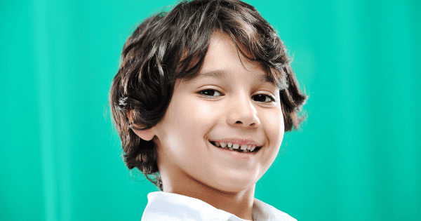 Young boy smiling at the camera with a dark green background.