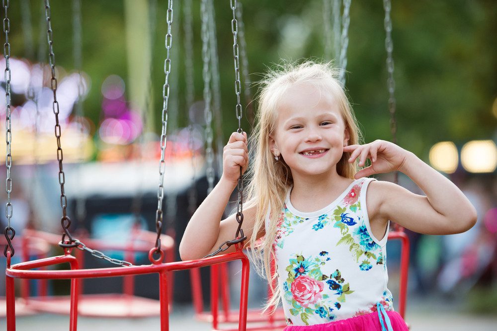 Cute little girl enjoing time at fun fair, chain swing ride, amusement park in summer