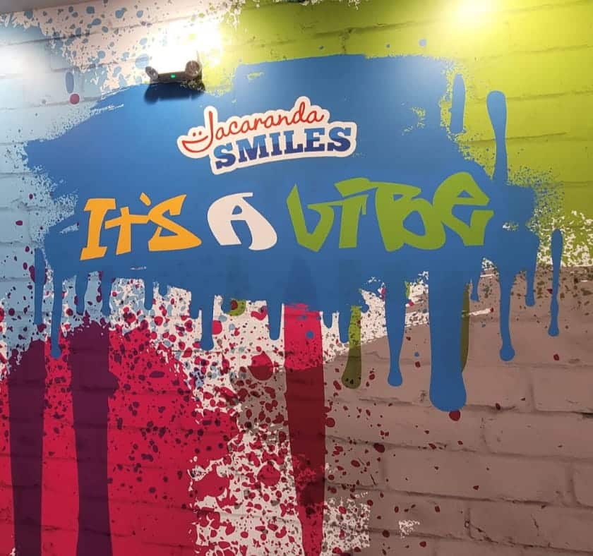 A colorful “It’s a Vibe” wall sign with Jacaranda Smiles branding inside the Plantation office.